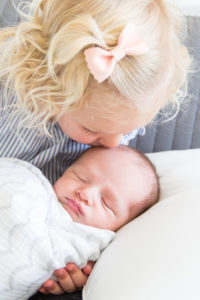 big sister kissing newborn baby's head