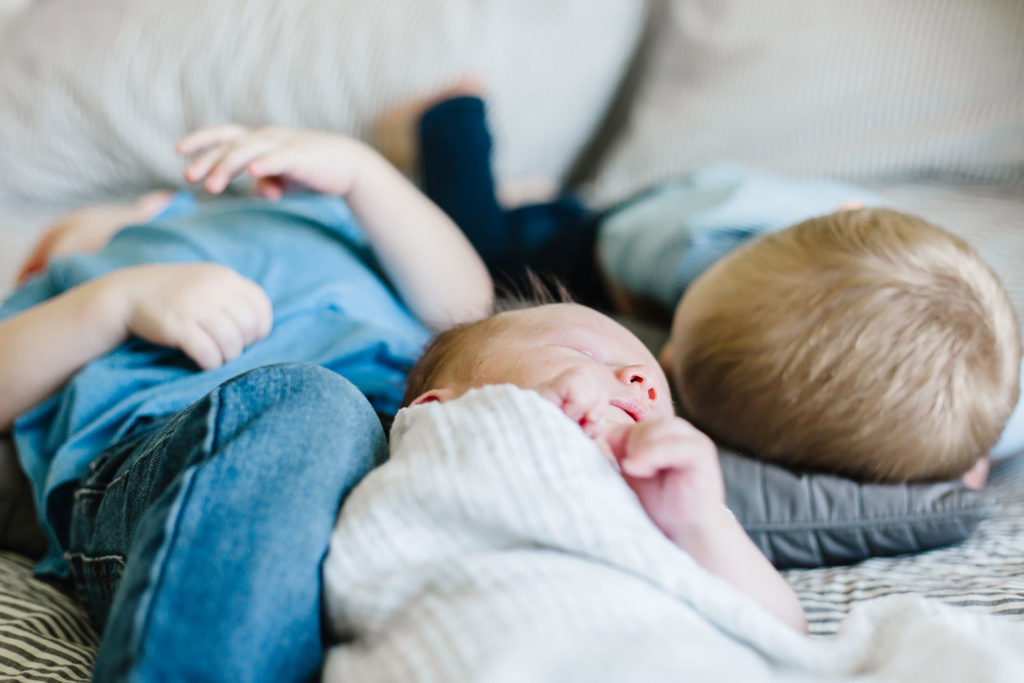 siblings all laying on the bed with newborn baby brother for in-home newborn session
