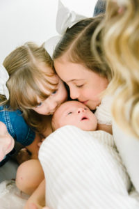 siblings kissing newborn baby head