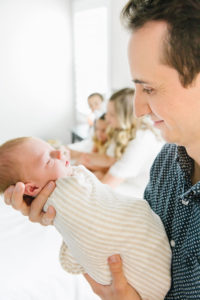 dad holding newborn while family is in the background