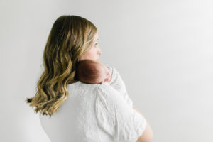 mom holding newborn looking out the window