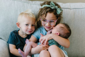 Sister and brother holding and snuggling newborn baby brother