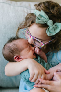 Sister kissing newborn brother on the forehead