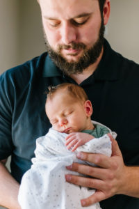 Dad holding newborn baby boy in front of him and looking down