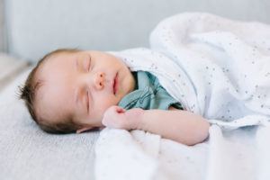 Newborn baby boy sleeping with one arm out of the swaddle